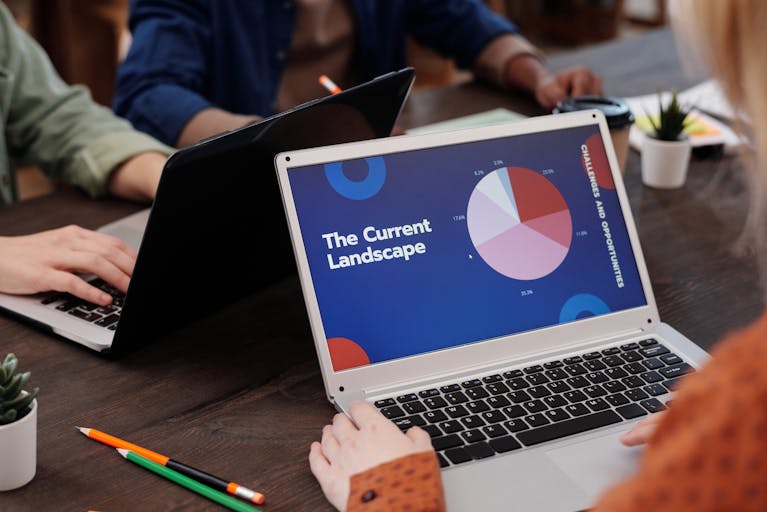 A team collaborates during a business meeting using laptops, analyzing data graphs.