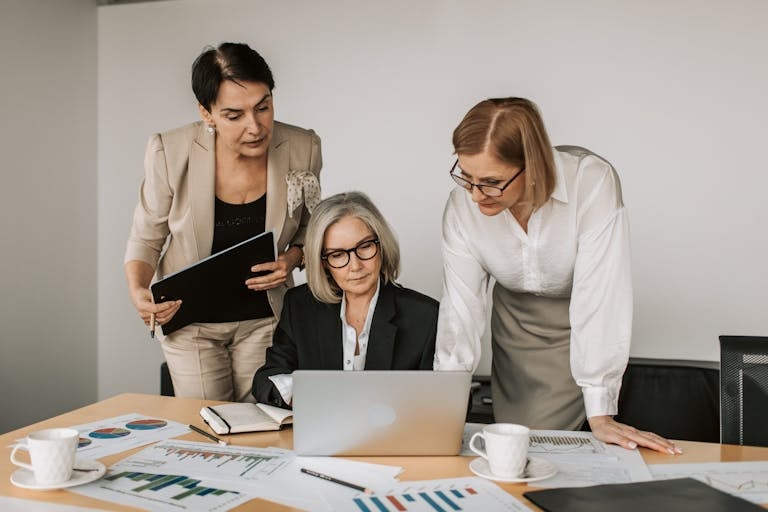Three women in a business meeting, discussing strategy with charts and laptop.